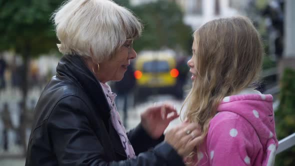 Side View Gorgeous Senior Grandmother Touching Hair of Cute Granddaughter Talking Outdoors