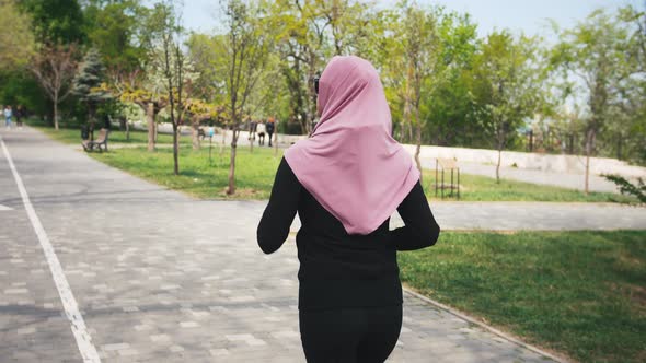 Backview of Young Modern Muslim Woman in Hijab Jogging in Green Park