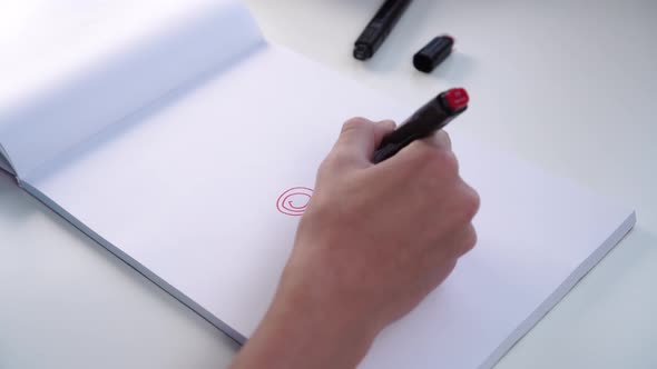 Hand of a teenager draws with felt-tip pen on a white blank sheet of an album