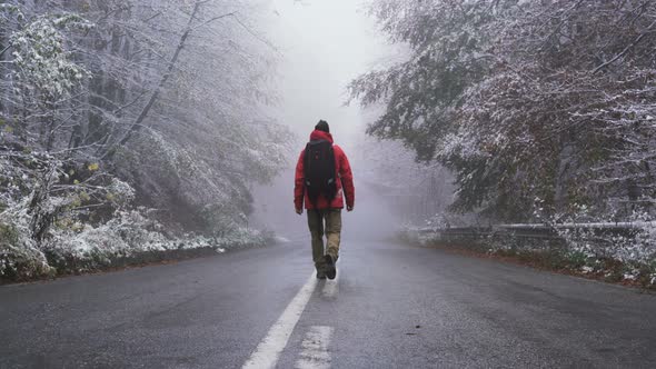 Back View of Male Tourist with Big Black Backpack Walking on Asphalt Road in The Winter, Looking