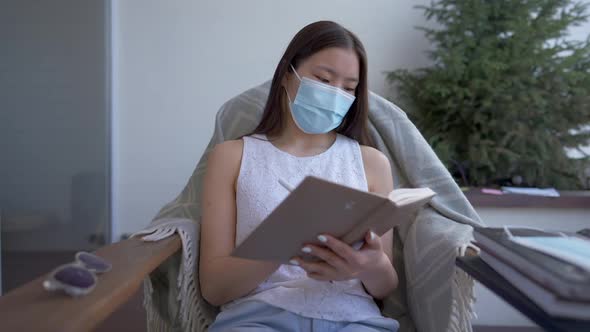 Portrait of Serious Charming Asian Woman in Face Mask Checking Business Ideas in Workbook Sitting in