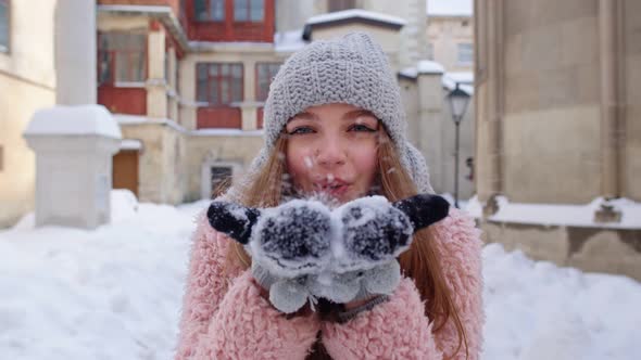 Young Woman Traveler Tourist Showing Snow in Hands Palms To Camera and Blowing It on City Street