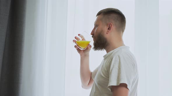 bearded man near the window drinking orange juice.  fresh squeezed orange juice