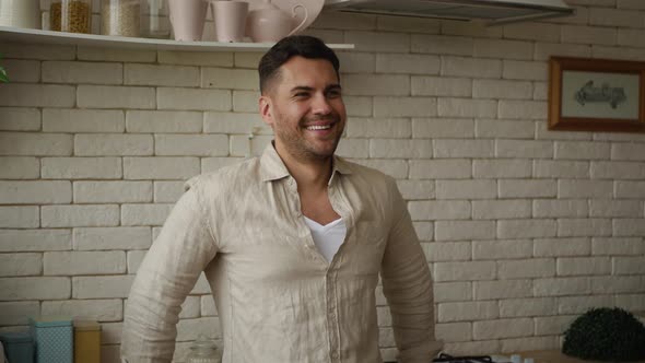 A handsome man on the background of the kitchen with someone talking and looking at the camera