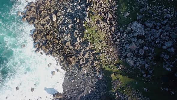 Aerial overhead shot of surf breaking on wild, rocky coast on a sunny day