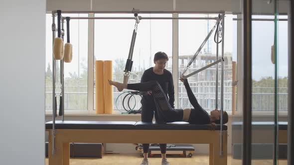 Wide Shot Portrait of Professional Personal Trainer Helping Caucasian Sportswoman with Pilates