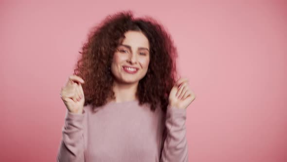 Beautiful Woman with Curly Hair Dancing with Head on Pink Studio Background.