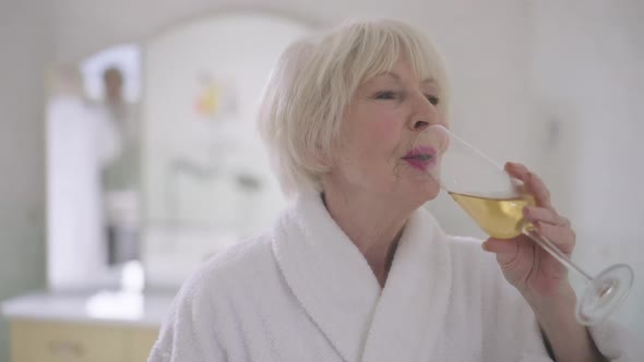 Portrait of Smiling Beautiful Senior Woman with Grey Hair Drinking Champagne in Slow Motion in