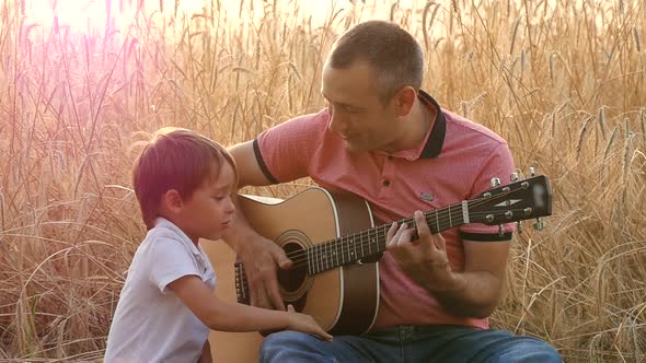 Happy Family: Father and Son Are Resting, Sitting on the Background of a Wheat Field. Father and