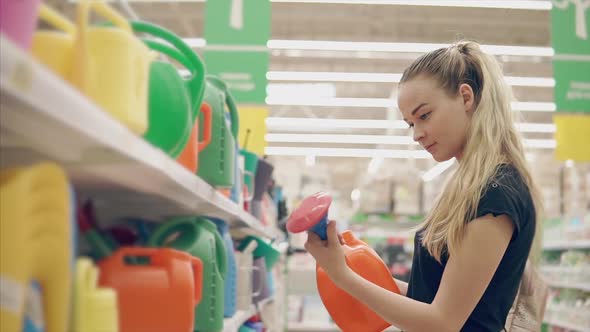 Young Woman is Watching a Plastic Watering Can for Gardening in a Store