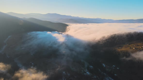 Aerial View of Vibrant Landscape of Foggy Clouds Covering Mountain Hills and Small Scattered Village