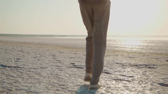 Slow Motion Rear View Woman's Feet and Back Girl Hiker Walking Along White Beach with Crystallized