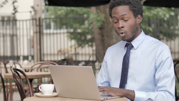 African Businessman in Shock By Results on Laptop in Outdoor Cafe