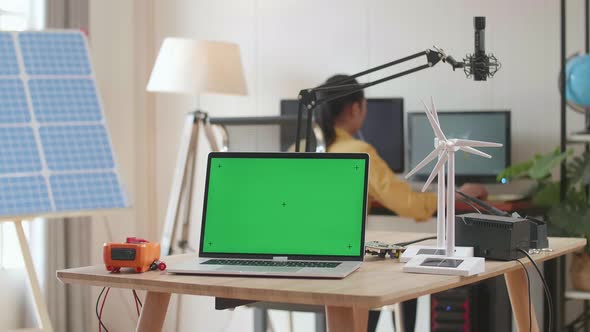 Asian Woman Working In Office That Has Solar Cell Next To The Green Screen Laptop And Wind Turbine