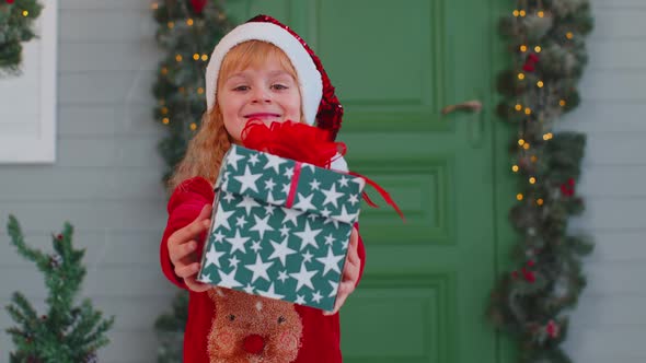 Joyful Toddler Child Girl Kid in Red Sweater Presenting One Christmas Gift Box Stretches Out Hands