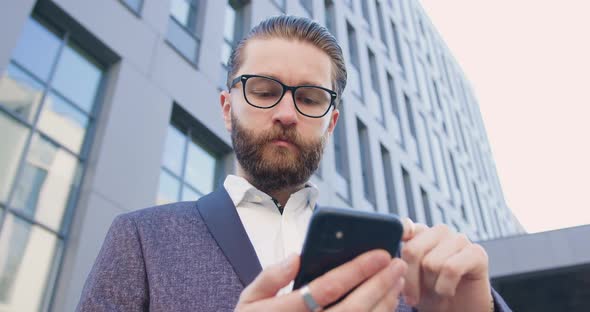 Man in Classy Clothes Using His Mobile Near Modern Big City building