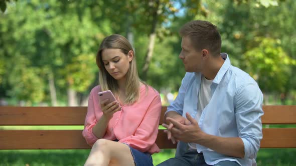 Young Woman Scrolling Phone Ignoring Man Hugging Her, Problems in Relationship