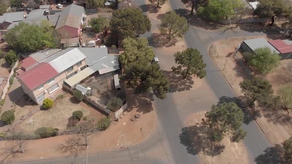 aerial follow shot of a car driving in a suburb crossing a small intersection