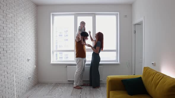 Happy Family with Little Baby Son in the Living Room in Front of the Window