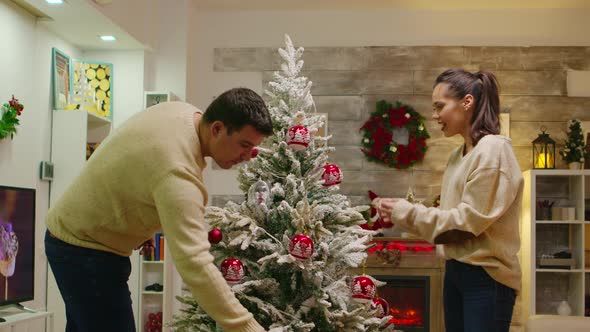 Young Couple Hangs Globes on Christmas Tree