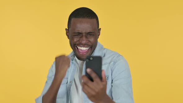 Young African Man Celebrating on Smartphone Yellow Background