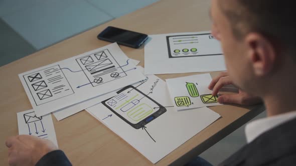 Young Man Designer Working with Blueprint Sitting at Table in Office Room.