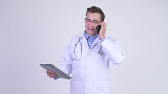 Young Happy Handsome Man Doctor Talking on the Phone While Using Digital Tablet