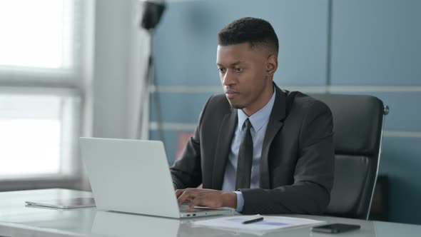 African Businessman Pointing at Camera while using Laptop in Office