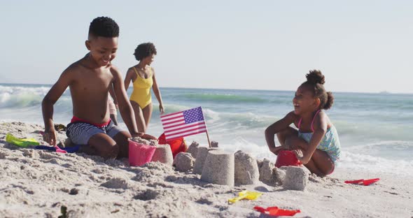 Smiling african american family building sandcastle with american flag on sunny beach