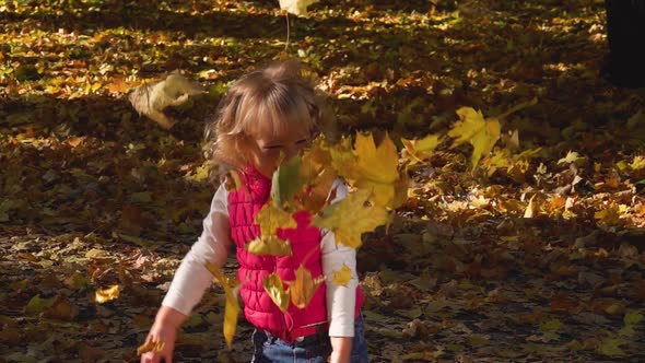 A Happy Little Girl in a Pink Vest Laughs and Tosses Up an Armful of Golden Fallen Leaves