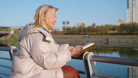 Middle Aged Caucasian Woman Reading the Book on Sunny Day Outdoors