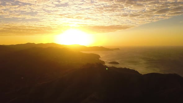 Aerial view of a bright yellow sunrise over a tropical mountain.