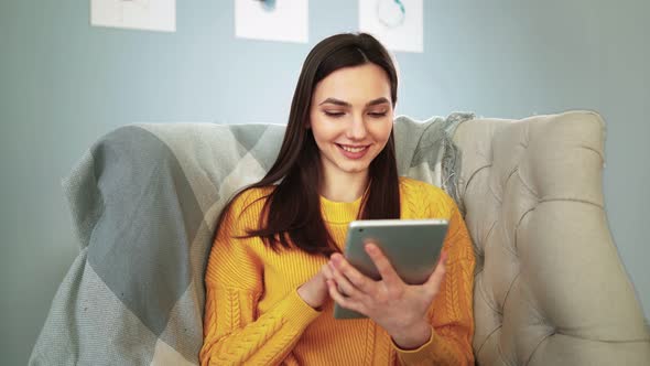 Woman Sitting on Cozy Sofa Smiles and Studies App on Digital Computer Tablet