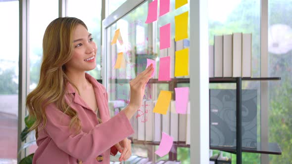 Young Creative businesswoman holding a marker and writing plan and share idea on glass wall with sti