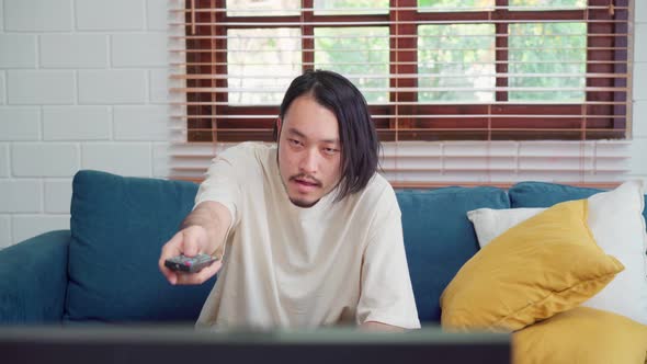 Asian man watching television in living room at home, male feeling happy lying on sofa.