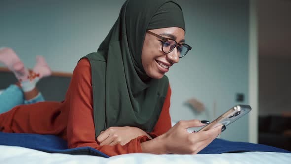 Smiling Muslim woman wearing eyeglasses typing on phone