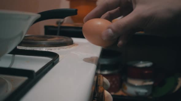 Egg cracked on the edge of a stove with the egg white dripping