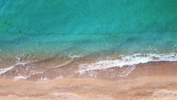 Top view on the waves of turquoise and clear sea water washing the sand on the shore.