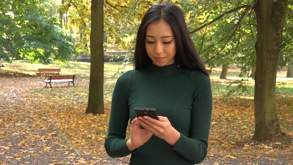 A Young Asian Woman Works on A Smartphone in A Park
