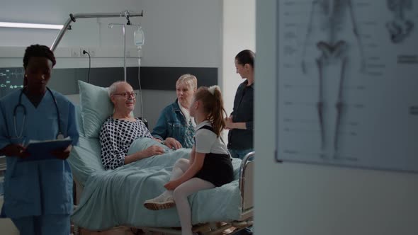 Senior Man Enjoying Chat with Niece at Visit in Hospital Ward Bed