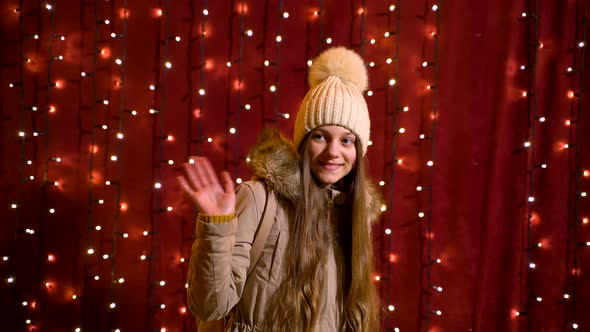 Cute teenager posing and waving in front of lights wall at Christmas market.