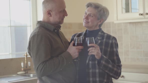 Old Couple Stand in the Kitchen with Wine Glass in Them Hands, Woman Try To Calm Down and Relax Her