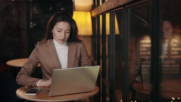 Focused Woman Typing on Laptop While Sitting at Cafe