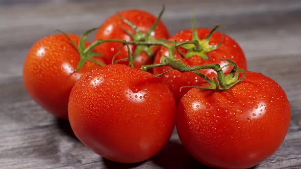 Appetizing Red Juicy Tomatoes on a Branch with Water Drops Lie on a Wooden Surface and Spin