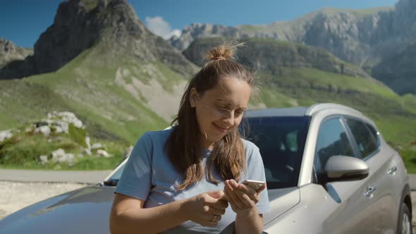 Millennial woman traveler looking at mobile app during a car summer trip against mountain