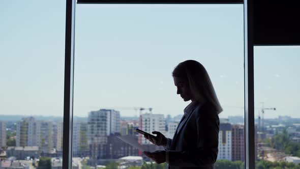 Silhouette of Business Woman Using Smartphone Holding Document Walking in Office