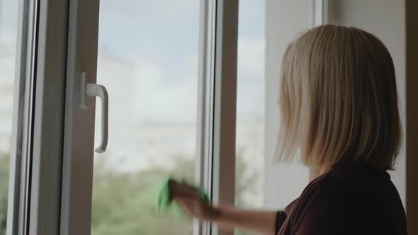 Side View A Woman Washes a Window in the Apartment of a Highrise Building