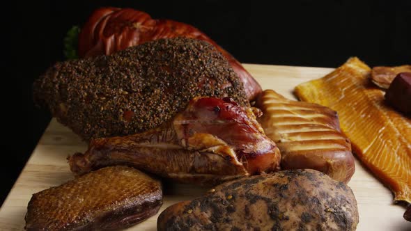 Rotating shot of a variety of delicious, premium smoked meats on a wooden cutting board 