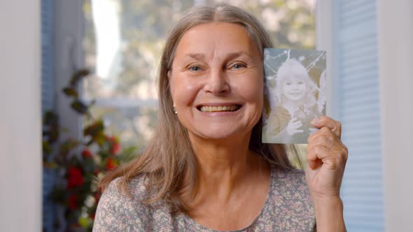 Attractive Retired Woman with Grey Hair Holding Her Photo As Little Girl