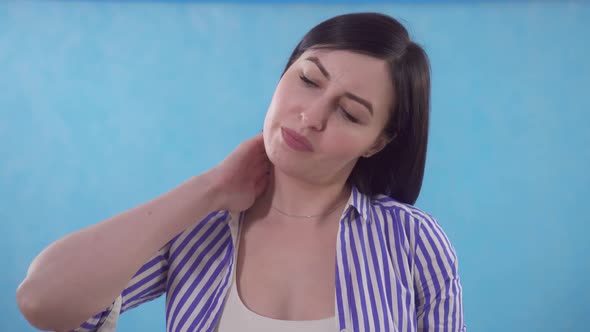 Young Woman Experiences Pain in Her Neck Standing on a Blue Background